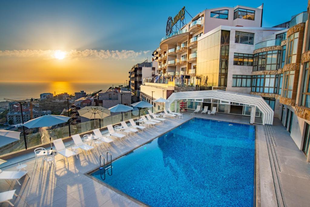 - une piscine sur le toit d'un immeuble avec un coucher de soleil dans l'établissement Maximus Hotel Byblos, à Byblos