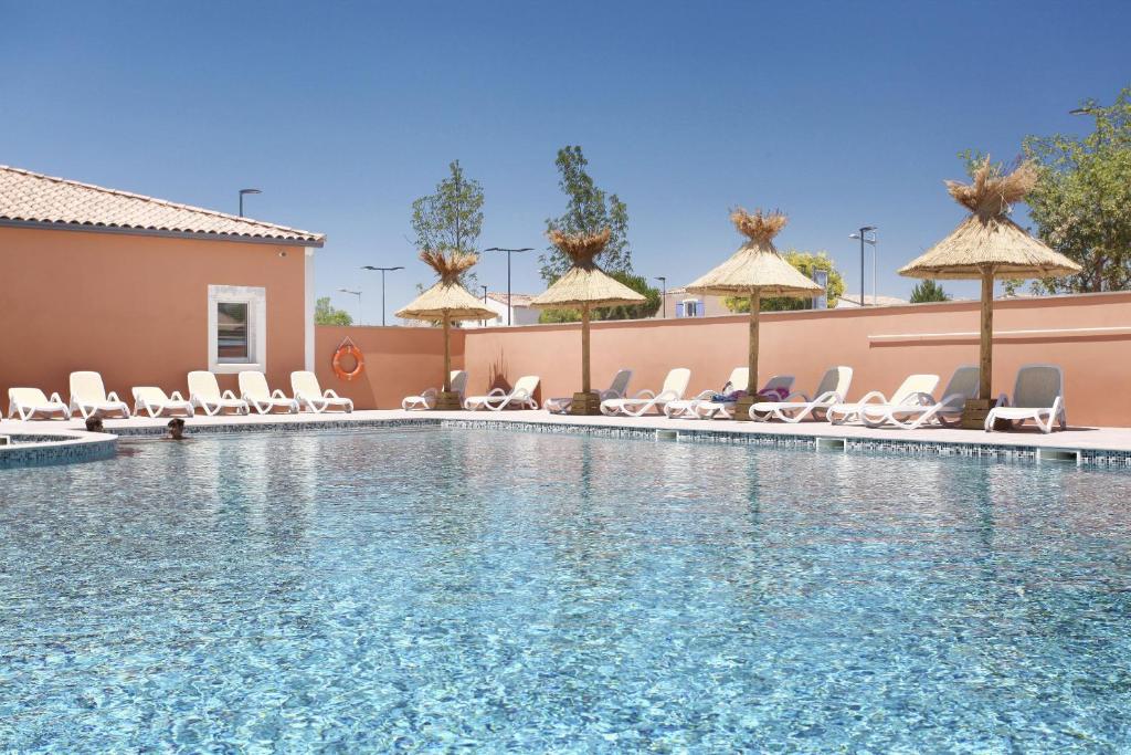 a swimming pool at a hotel with chairs and umbrellas at Résidence Odalys Fleur de Sel in Aigues-Mortes