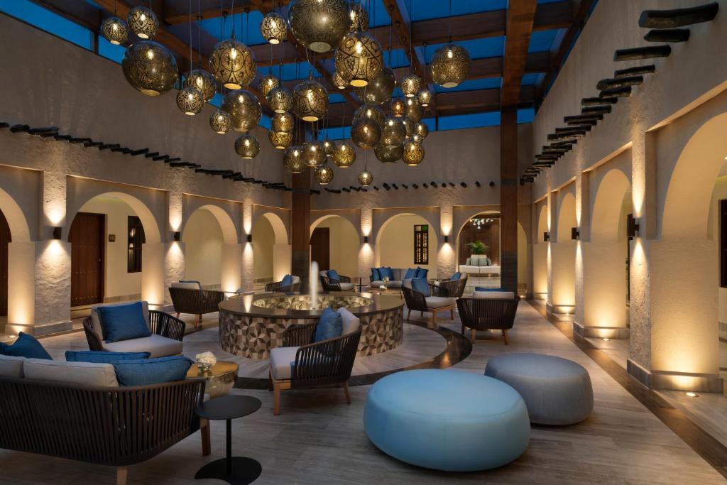 a lobby with chairs and tables and chandeliers at Souq Al Wakra Hotel Qatar By Tivoli in Doha