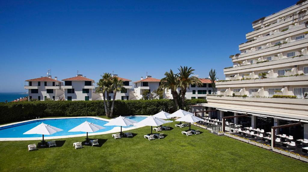 a pool with chairs and umbrellas in front of a building at Melia Sitges in Sitges