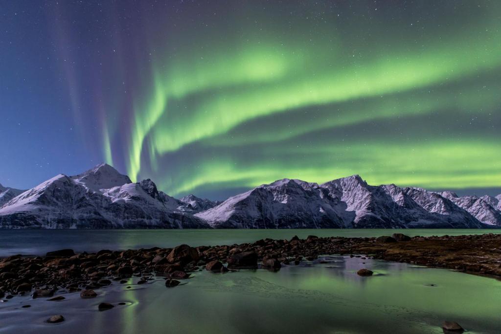 een noorderlicht over een bergketen met een waterlichaam bij Lyngenfjord,Odins Hus in Olderdalen