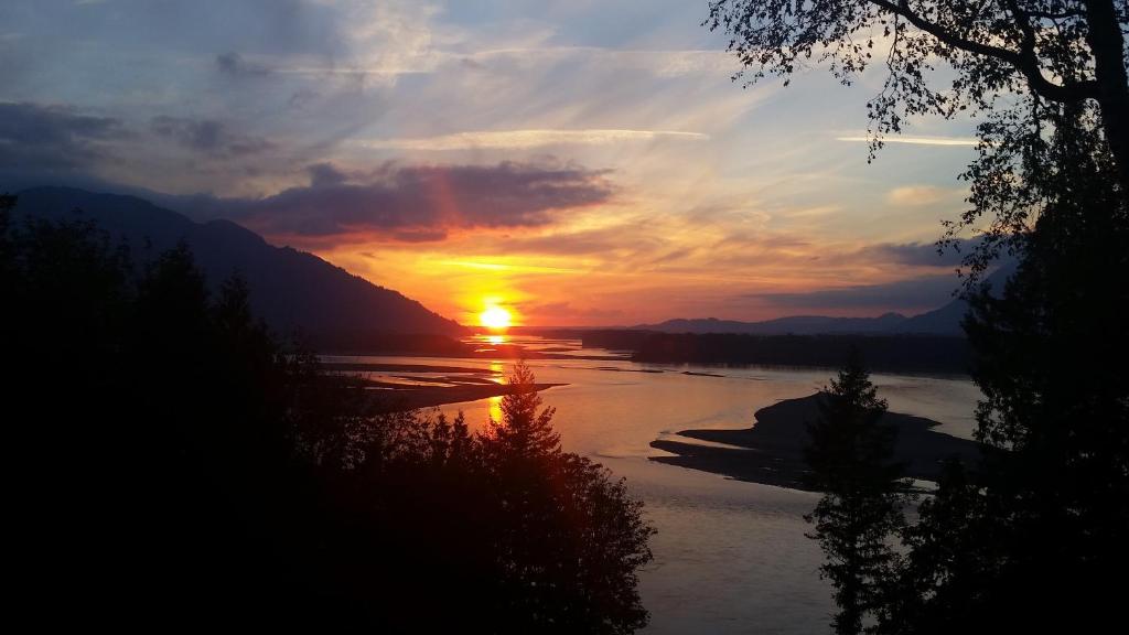 a sunset over a river with the sun setting at The Fraser River's Edge B&B Lodge in Chilliwack