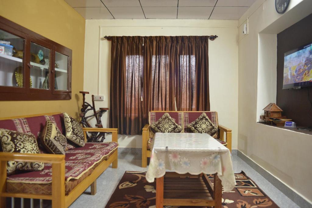 ein Wohnzimmer mit einem Tisch, Stühlen und einem Fenster in der Unterkunft Agasthya Homestay - With Kitchenette in Madikeri