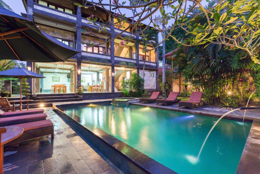 a swimming pool with chairs and a house at Wenara Bali Bungalows in Ubud