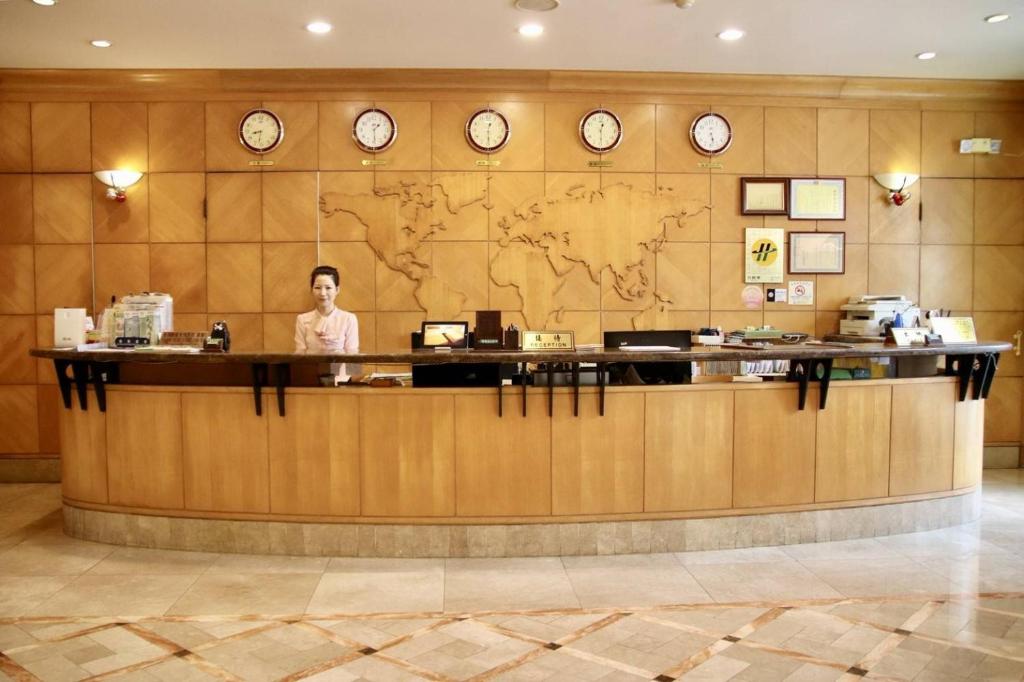 a woman standing at a counter in a lobby with clocks at Oriental Hotel in Tainan