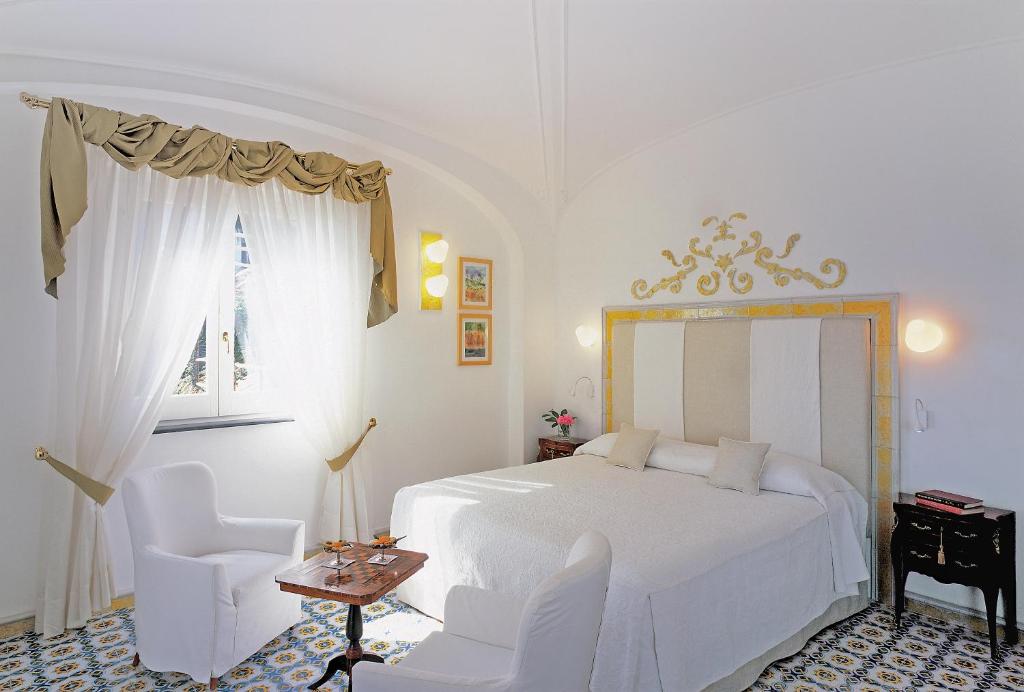 a white bedroom with a bed and two chairs at Hotel Santa Caterina in Amalfi