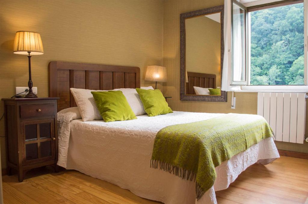 a bedroom with a bed with green pillows and a mirror at Hotel del Alto Sella in Amieva