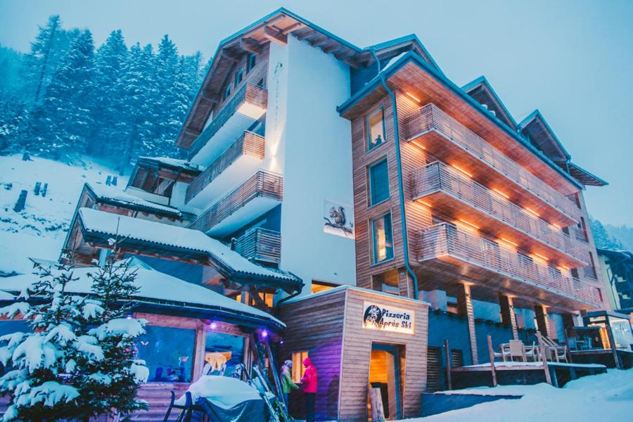 a large building in the snow with a tree in front at Hotel Scoiattolo in Tesero