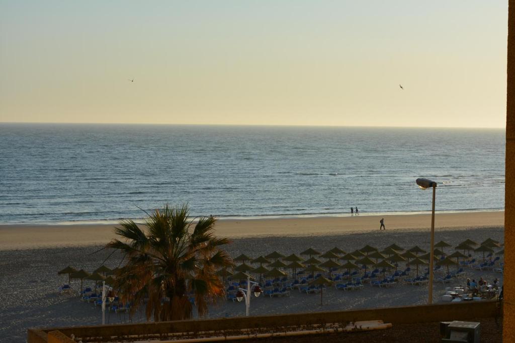 a beach with chairs and umbrellas and the ocean at Apartamento Playa Victoria - Cádiz in Cádiz
