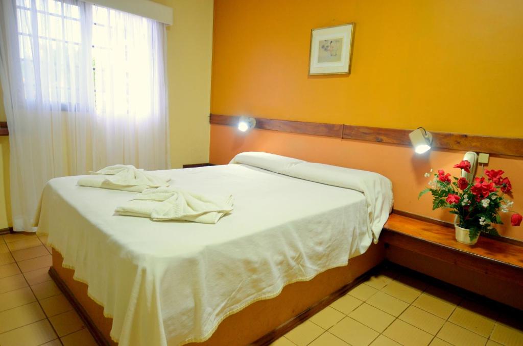 1 dormitorio con 1 cama con sábanas blancas y un jarrón de flores en Hostería Casa Blanca Iguazú en Puerto Iguazú