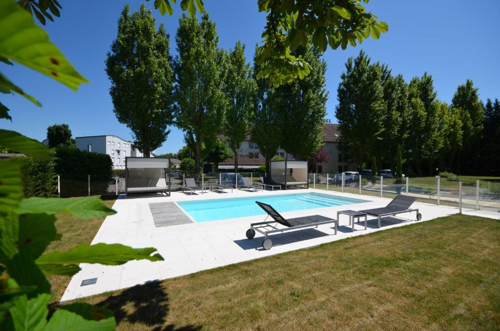 a swimming pool with two benches next to a yard at Kyriad Dijon Est Mirande in Dijon