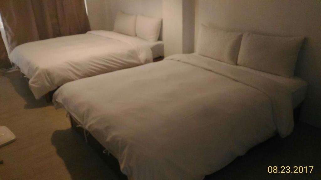 two beds in a hotel room with white sheets and pillows at Haogong Hotel in Taichung