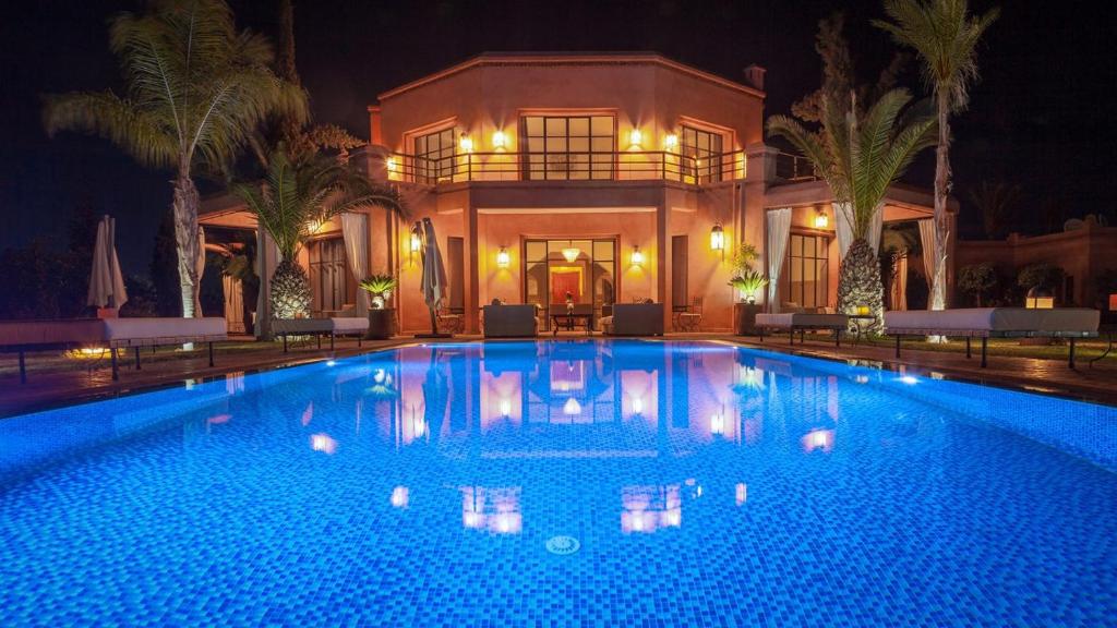 a large swimming pool in front of a house at night at Palmeraie Dar Atlas - Luxury Houses in Marrakesh