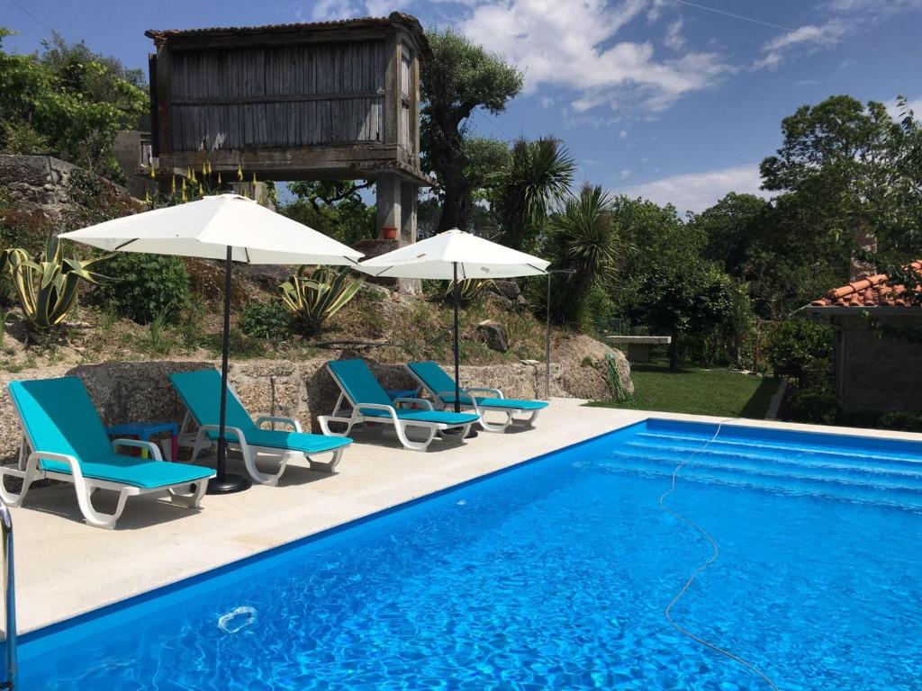 una piscina con sedie e ombrelloni accanto a una casa di Casa Cima de Vila a Vieira do Minho