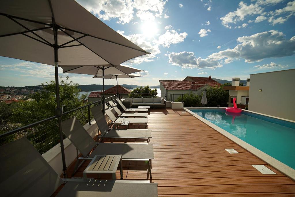 a deck with chairs and umbrellas next to a swimming pool at Apartments Gazebo in Trogir