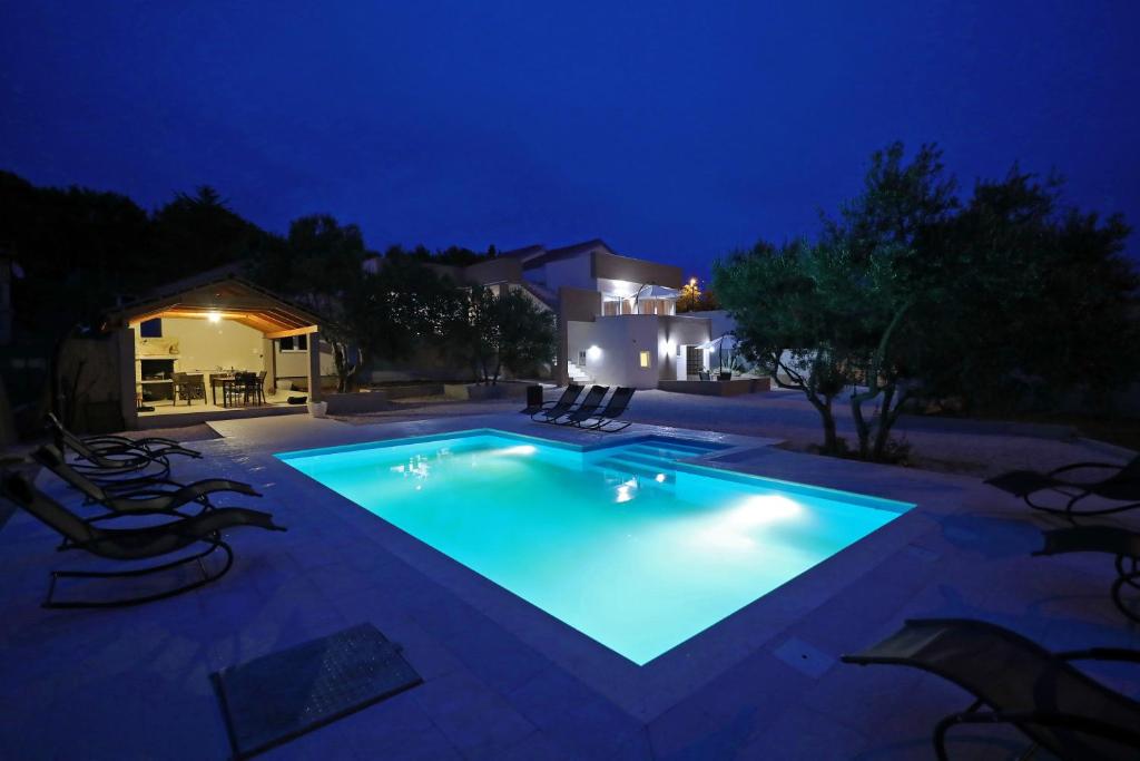 a swimming pool at night with chairs around it at Apartmani Olivia in Bibinje