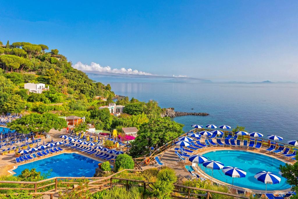 an aerial view of two pools with umbrellas and the water at Hotel Oasi Castiglione in Ischia