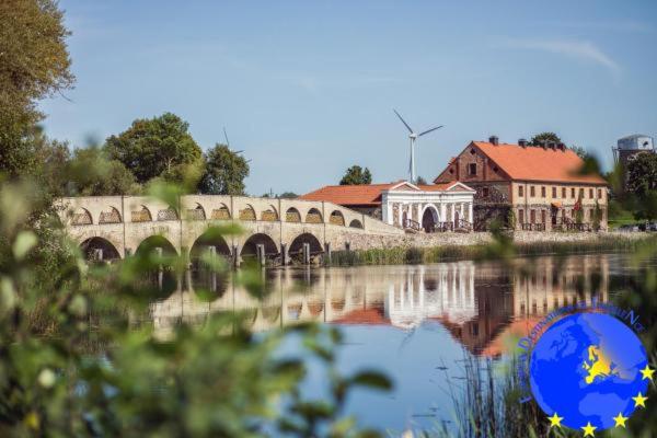 a bridge over a body of water with a building at Pakruojis Manor Hotel Miller's house in Pakruojis