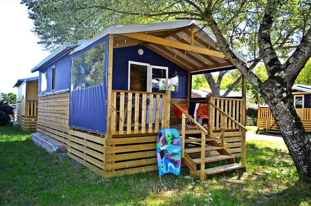 a blue and wooden cabin with a staircase next to a tree at Camping Routes du Monde ATC La Hume-Arcachon in Gujan-Mestras