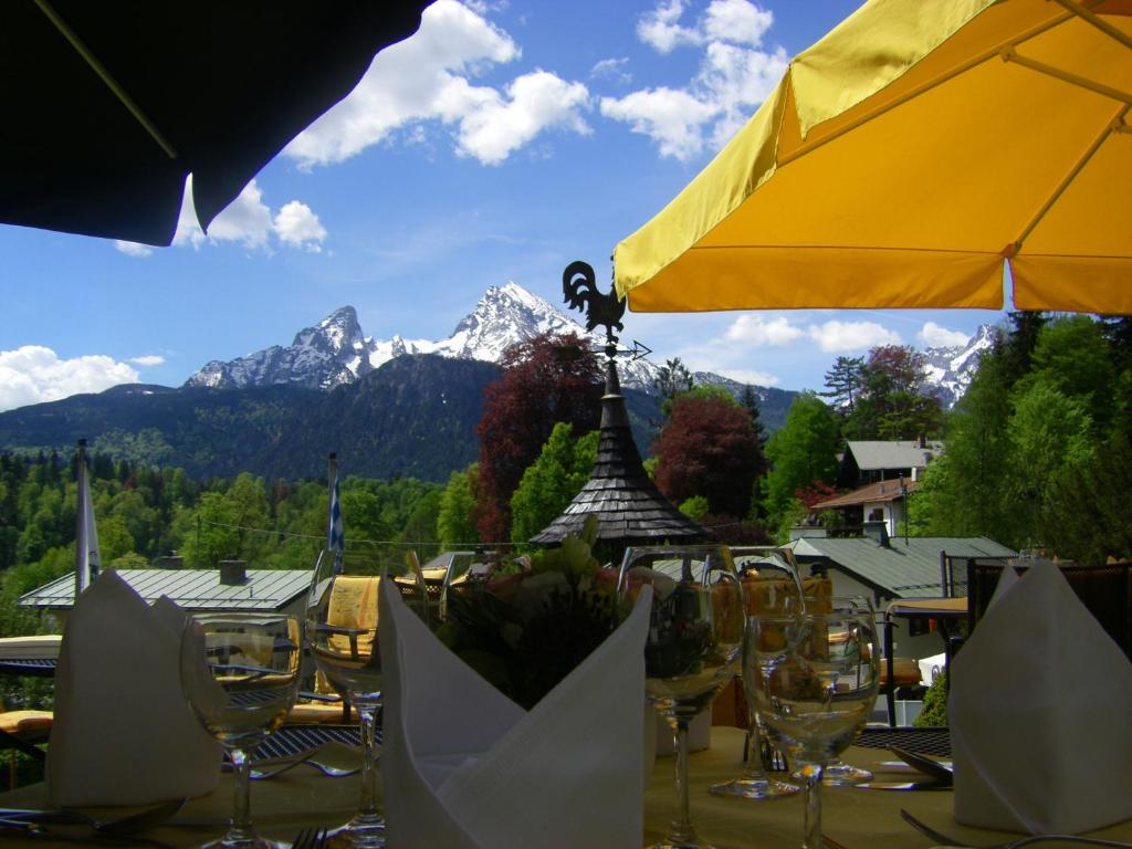 a table with glasses and a yellow umbrella and mountains at Alpenhotel Kronprinz in Berchtesgaden