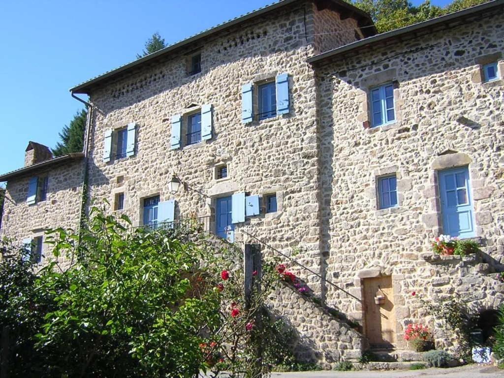 a large stone building with blue windows and flowers at Mas Casta Néa in Thueyts