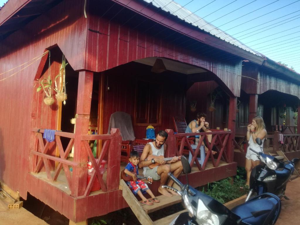 un groupe de personnes assis à l'extérieur d'une maison rouge dans l'établissement Bee Bee's Chalets home stay and trekking, à Banlung