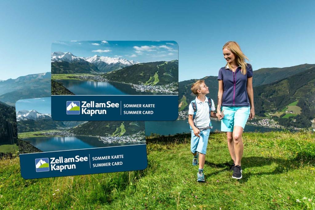 a woman and child walking on a hill with a lake and mountains at Hotel Gasthof Mitteregger in Kaprun