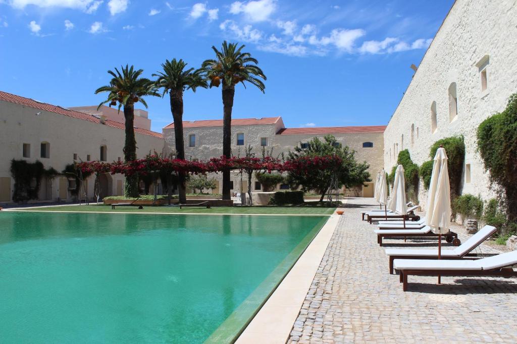 a swimming pool with chairs and palm trees next to a building at Convento das Bernardas AZ in Tavira