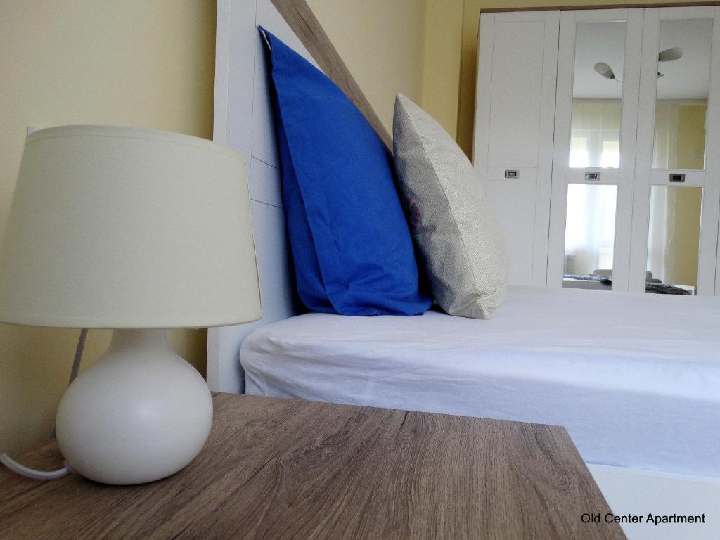 a bed with blue pillows and a table with a lamp at Old Center Apartment in Ruse