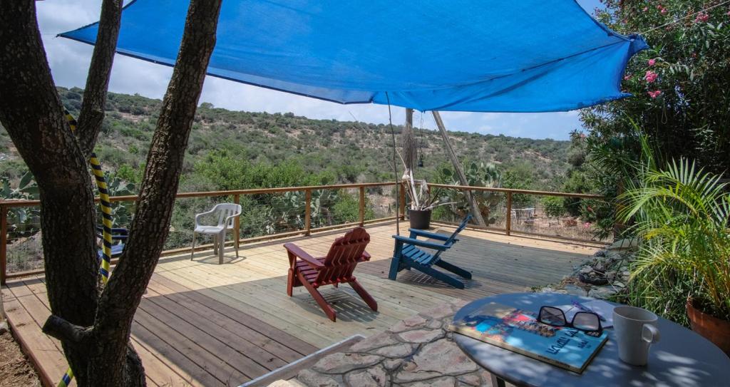 eine Terrasse mit einem blauen Regenschirm, einem Tisch und Stühlen in der Unterkunft Natural Reserve Apartment in Zichron Ja’akow
