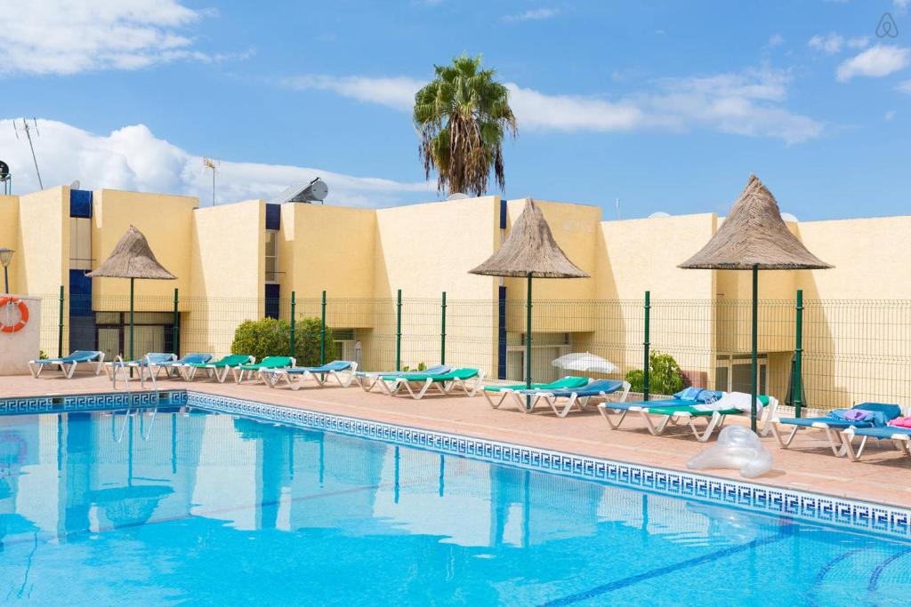 una piscina en un hotel con sillas y sombrillas en Cortijo en Playa de las Americas