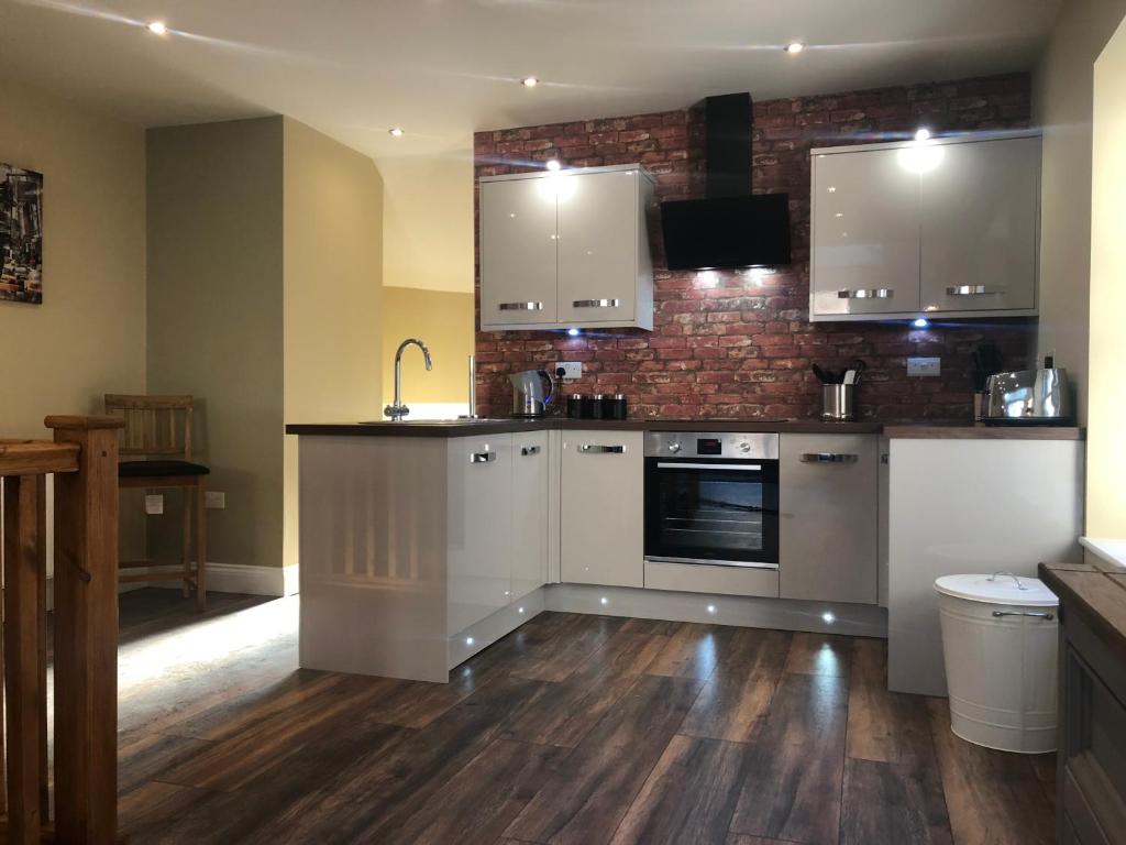 a kitchen with white cabinets and a brick wall at HomeArms Cottage in Eyemouth