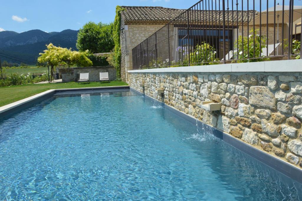 uma piscina com uma parede de pedra e uma fonte de água em Les Gîtes Du Clos D'Olea em Oppède