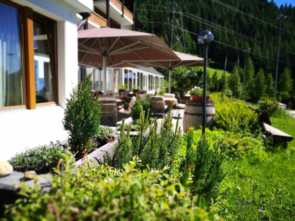 un jardín con plantas, una sombrilla y un edificio en Hotel Hubertus, en Obergesteln