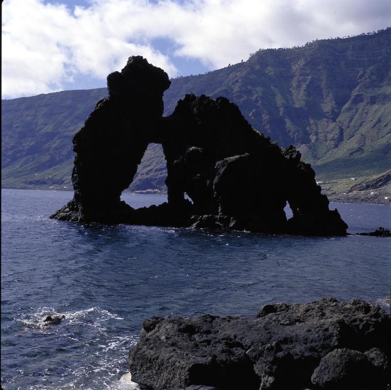 a rock in the water with mountains in the background at Parador de El Hierro in Las Casas