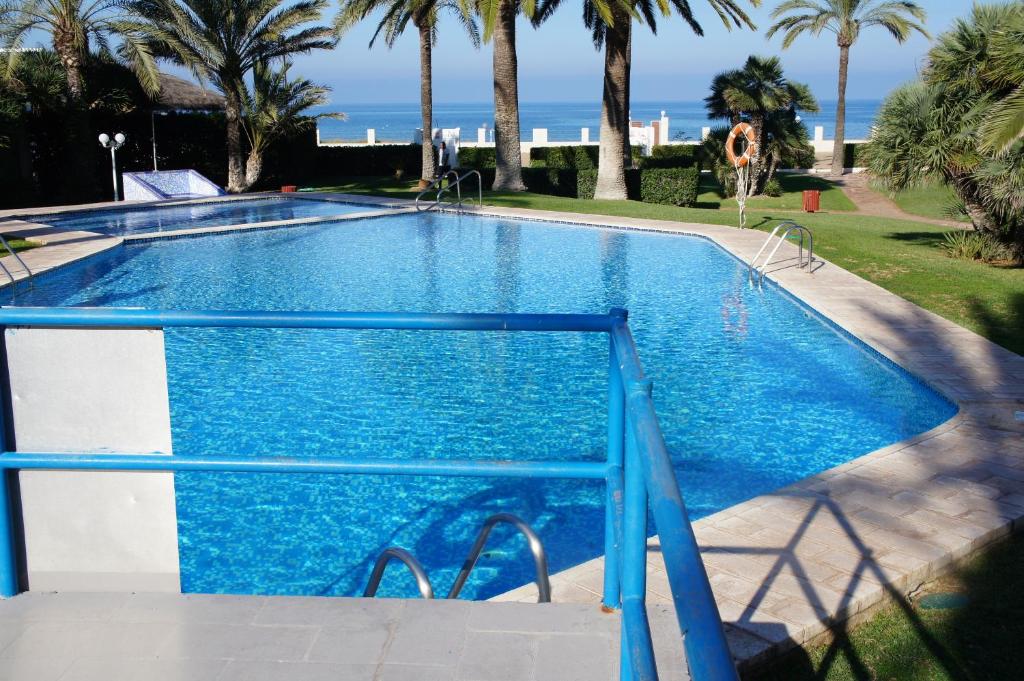 une grande piscine bleue avec des palmiers et l'océan dans l'établissement Gaby Albatros, à Dénia