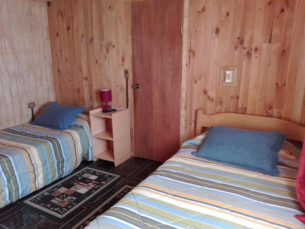 two beds in a room with wooden walls at Hospedaje Los Calafates in Ancud