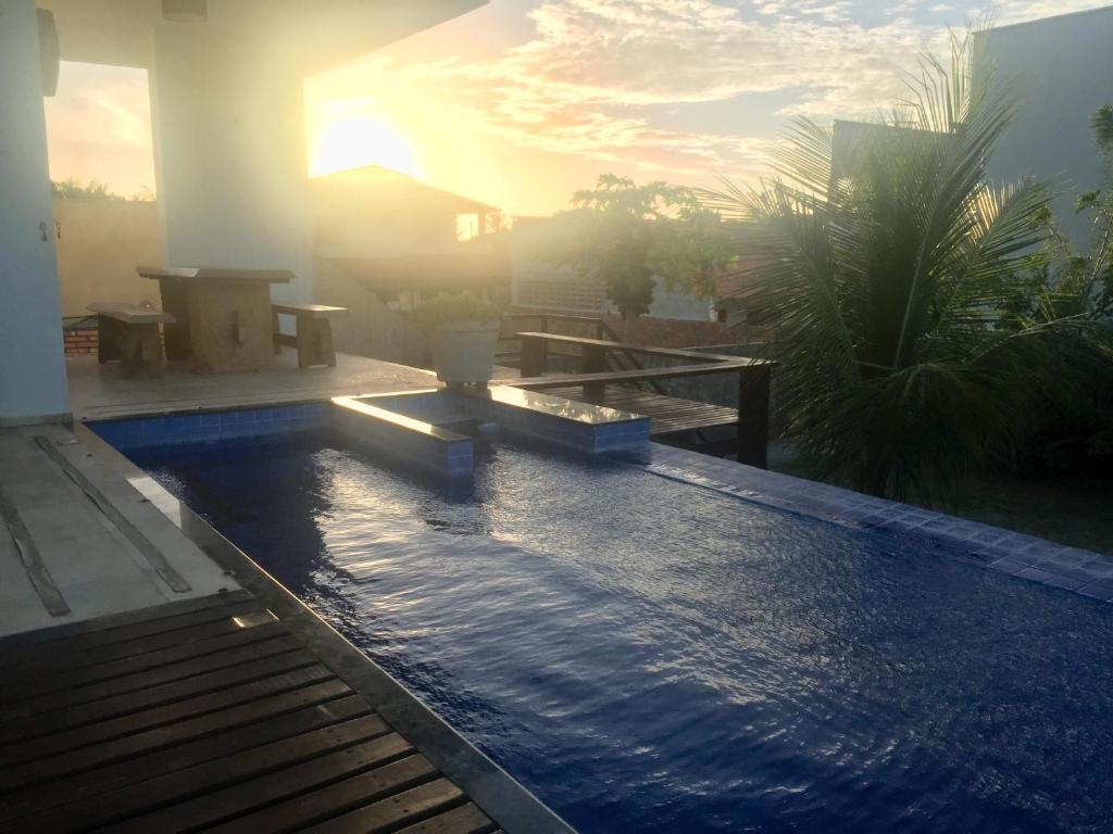 a swimming pool with the sun setting behind a house at Kite'll Out - Casa Flecheiras in Flecheiras