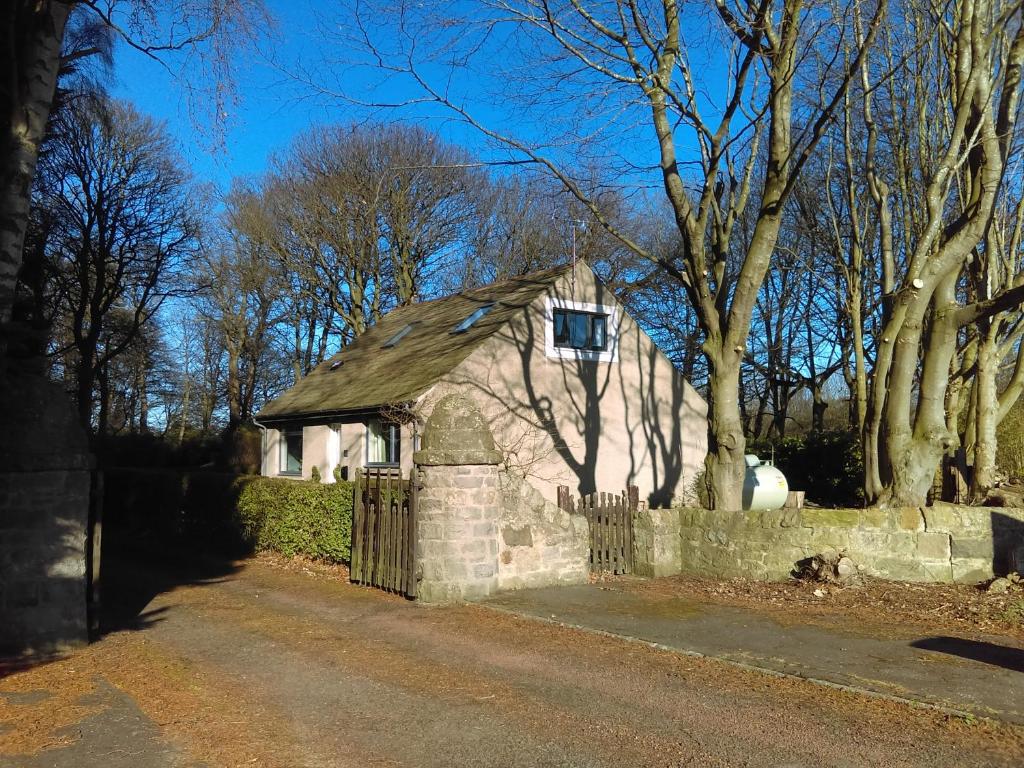 uma pequena casa de pedra com cerca e árvores em Lowood Cottage em Edinburgo