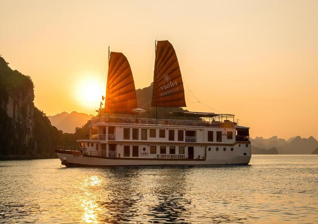 a boat with two sails in the water at sunset at Heritage Line Violet Cruise - Halong Bay & Lan Ha Bay in Ha Long