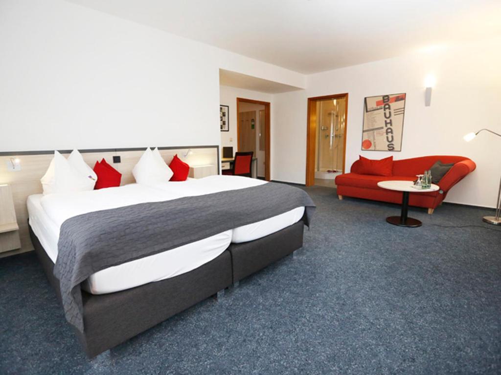 Cette chambre comprend un grand lit et un canapé rouge. dans l'établissement Hotel 7 Säulen GmbH, à Dessau