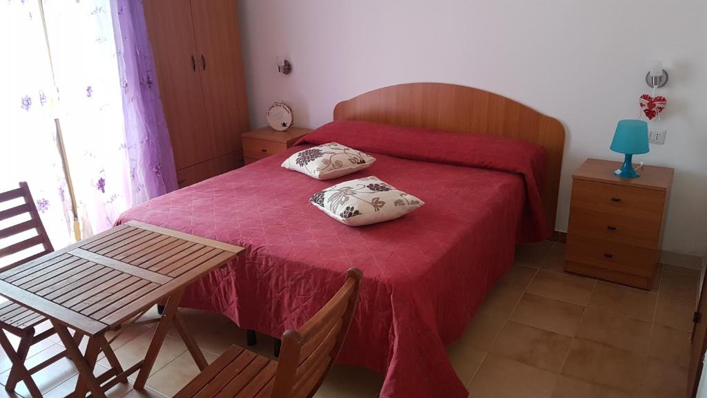 a bedroom with a red bed with a table and a chair at Cortili del Mar in Torre San Giovanni Ugento