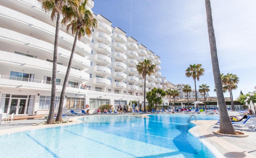 a swimming pool with palm trees in front of a building at BLUESEA Gran Playa in Sa Coma