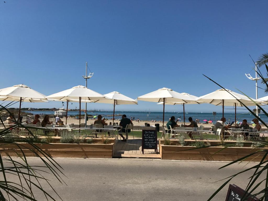 people sitting at tables with umbrellas at the beach at Hôtel Café Miramar in Le Grau-du-Roi