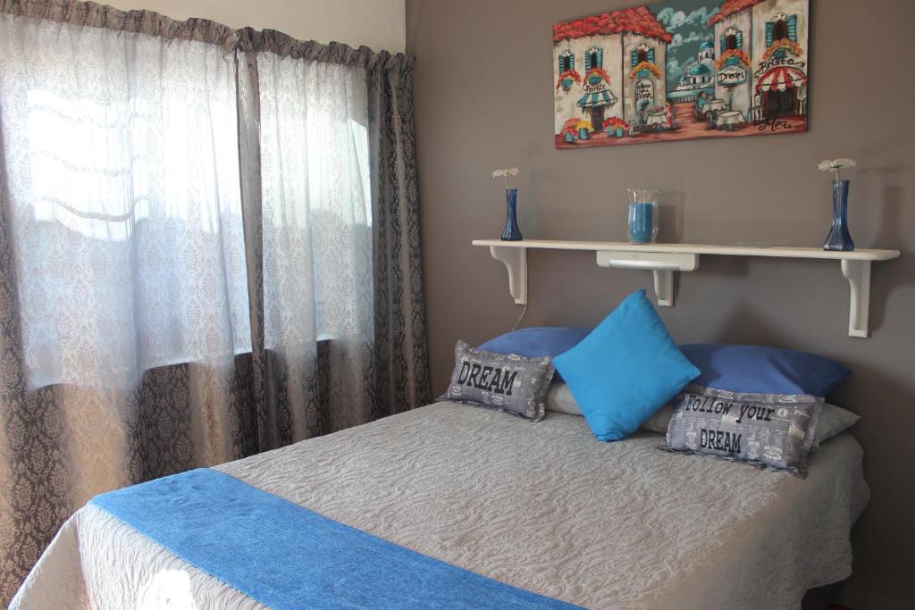 a bedroom with a bed with blue pillows and a window at PhysEQFiT Guesthouse & Spa in Centurion