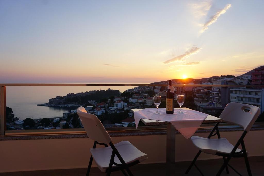 a table with wine glasses on a balcony with the sunset at Molla Apartments in Ulcinj