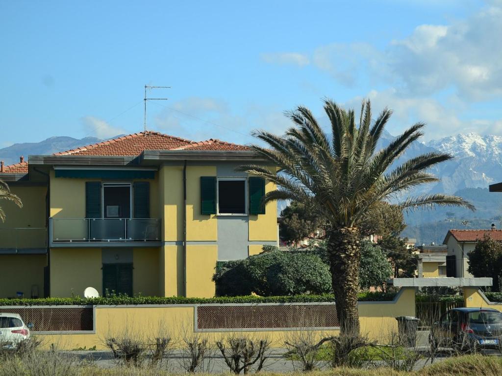 una casa gialla con una palma e montagne sullo sfondo di Cozy Holiday Home with Terrace in Carrara a Carrara