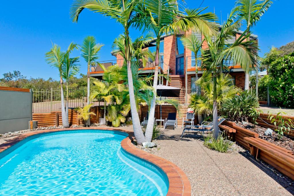 a swimming pool in front of a house with palm trees at Panorama Beach House in Bonny Hills