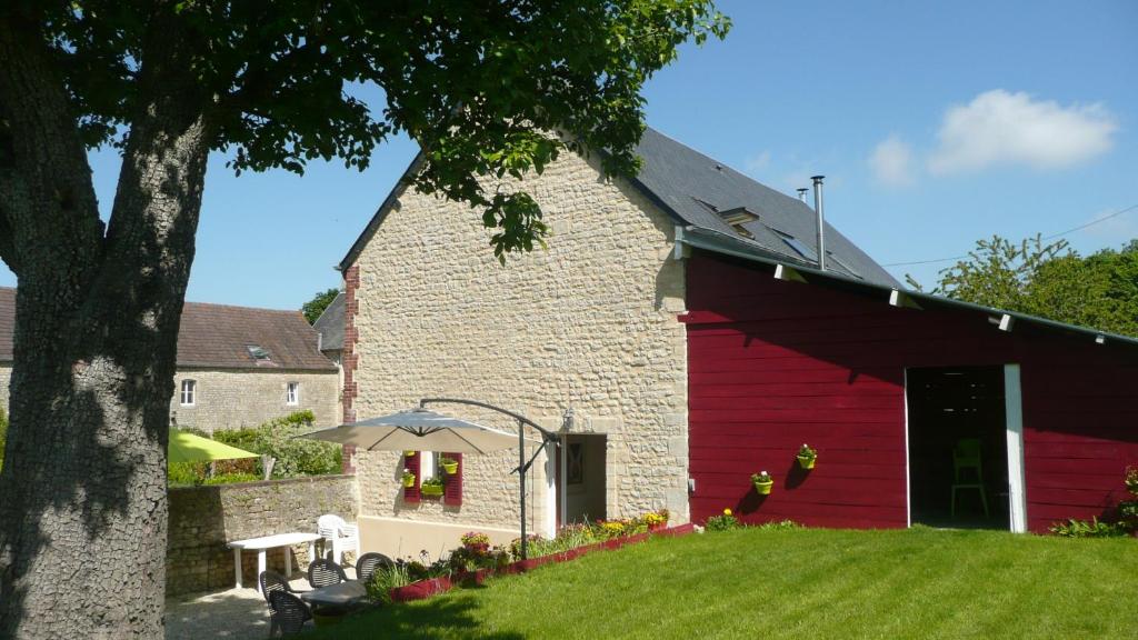 a red barn with a table and an umbrella at Gite de la Cour Vautier in Mandeville-en-Bessin