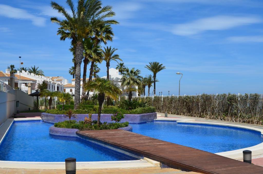 a swimming pool with a wooden deck and palm trees at Apartamentos Punta Cormorán V.v. in La Manga del Mar Menor